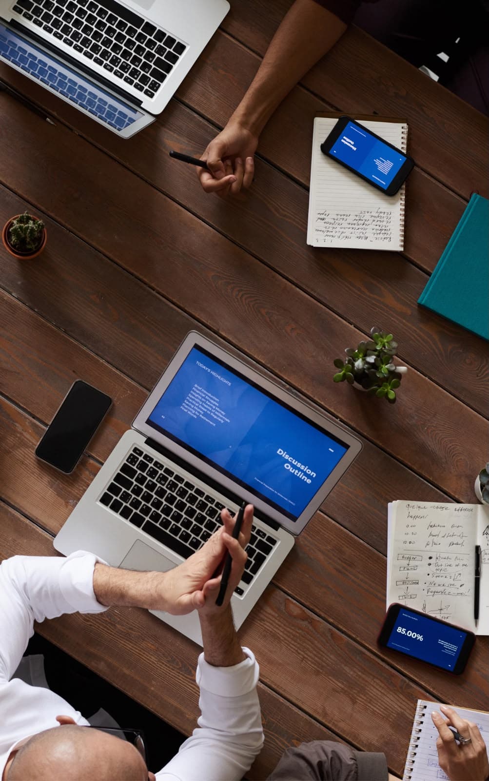 Top-down view of a team meeting around a wooden table with laptops and notes